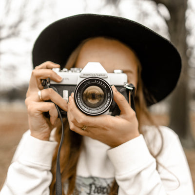 Lady wearing a hat and white jumper pointing camera at the viewer