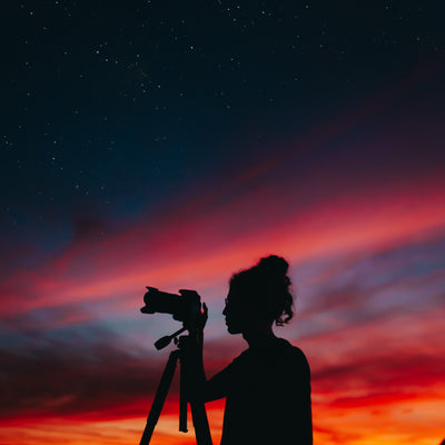 Silhouette of girl with tripod and camera against sunset backgroud