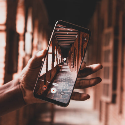 Hand holding a phone, showing camera and photograph of alleyway