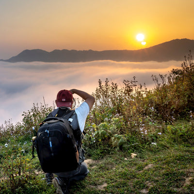 Man taking a photograph of a sunset over a mountain