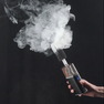 Hand holding a fog machine device emitting white smoke against a black background