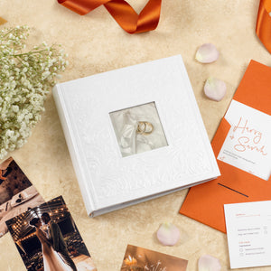 white wedding photo album with rings on table surrounded by wedding photographs